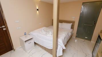 A hotel room with a bed, a nightstand, a wall-mounted light, a door, and a mirror.