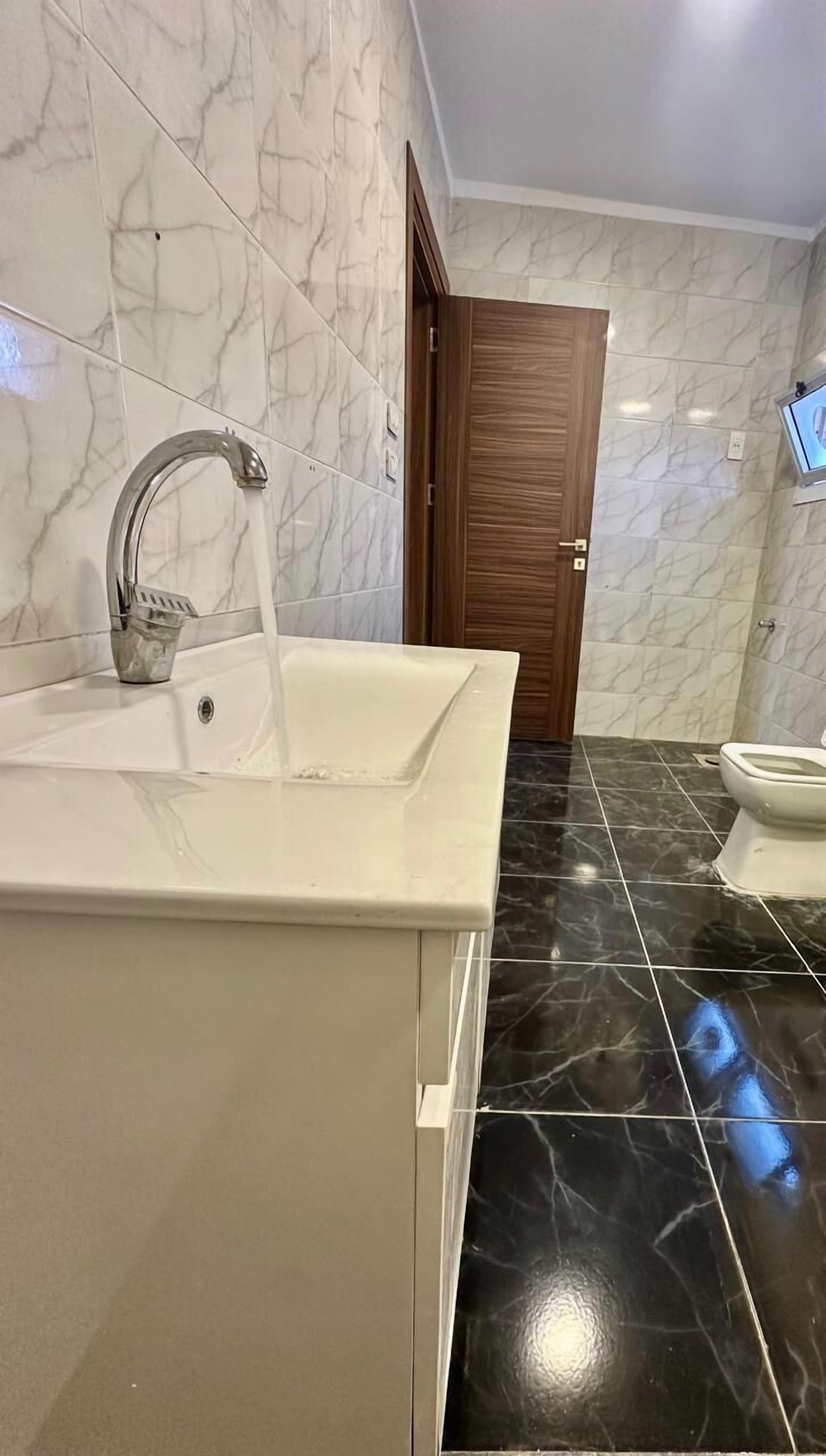 A bathroom with a white sink, a mirror, and a toilet. The floor is tiled with black and white marble.