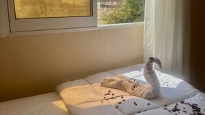 A bed with a swan-shaped pillow and scattered rose petals, a window with a view of a pyramid, and a curtain partially drawn. -  Pyramids Express View Inn  (Giza)