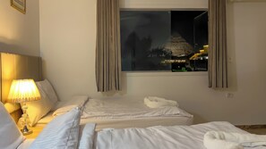 A hotel room with two beds, a nightstand with a lamp, and a window with curtains.