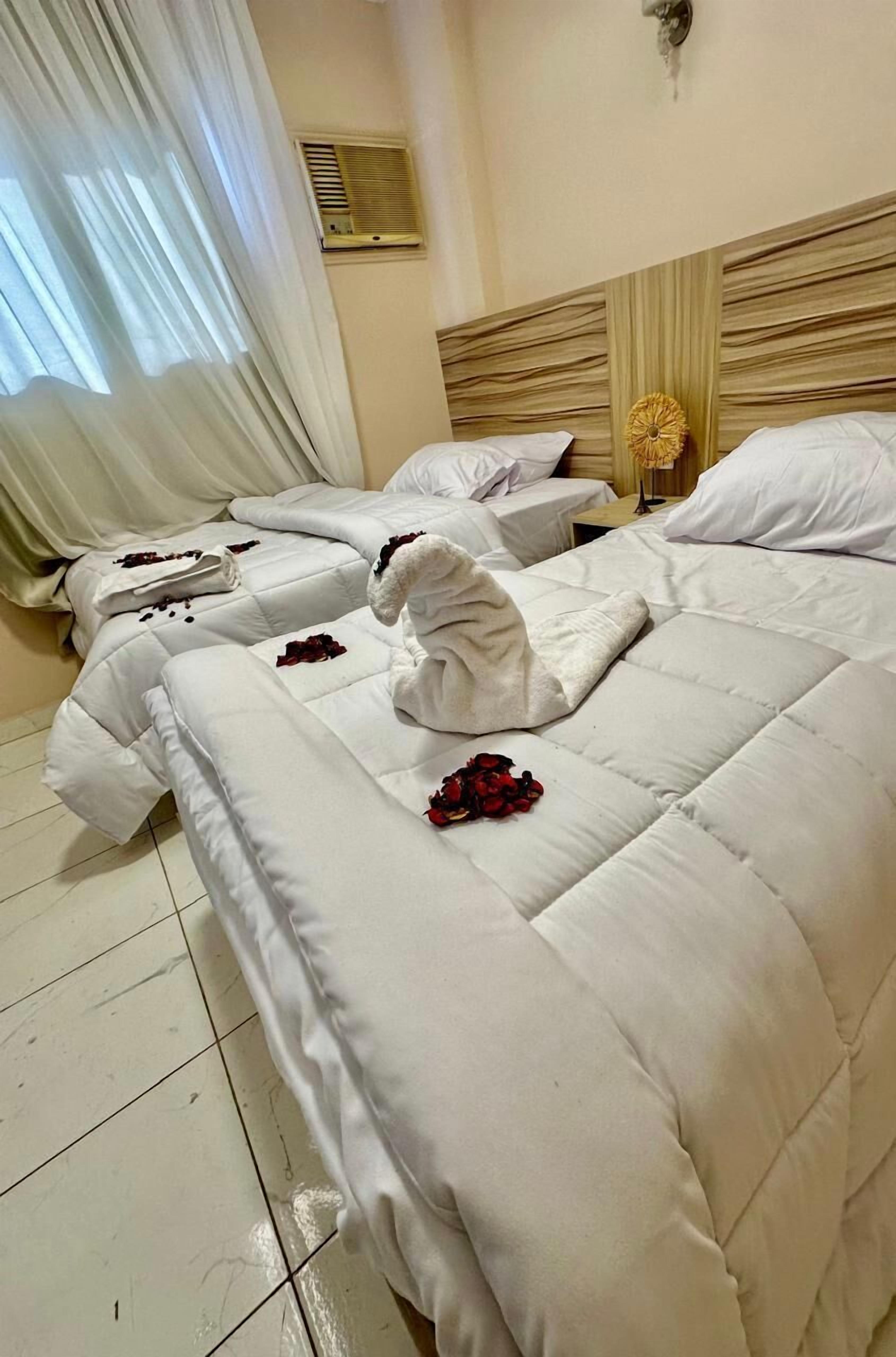 A hotel room with two beds, each with white linens and rose petals.