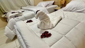 A hotel room with two beds, each with white linens and rose petals.