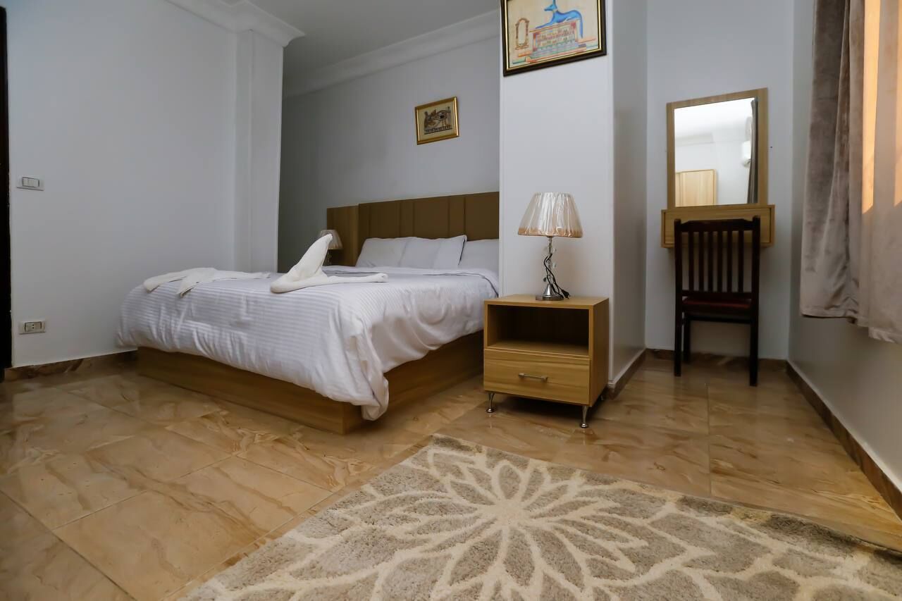 A neatly arranged hotel room with a bed, bedside table, lamp, chair, and a decorative rug.
