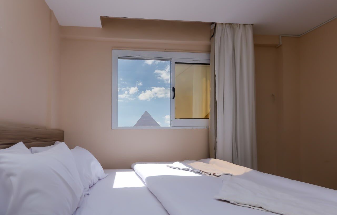 A hotel room with a bed, a window with curtains, and a view of a building outside.
