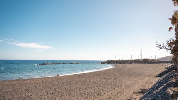 A beach with a rocky breakwater, calm sea, and clear sky.