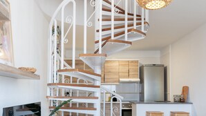 A modern kitchen with a spiral staircase, wooden cabinets, and a stainless steel refrigerator.
