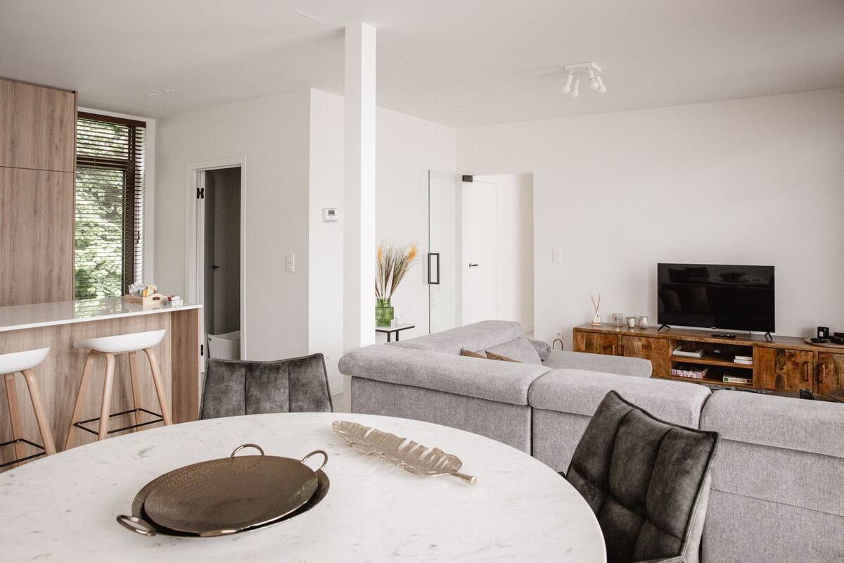 A modern living room with a grey sofa, a round dining table, and a TV on a wooden cabinet.