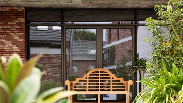 Een houten bank voor een gebouw met grote ramen en plantenpotten.