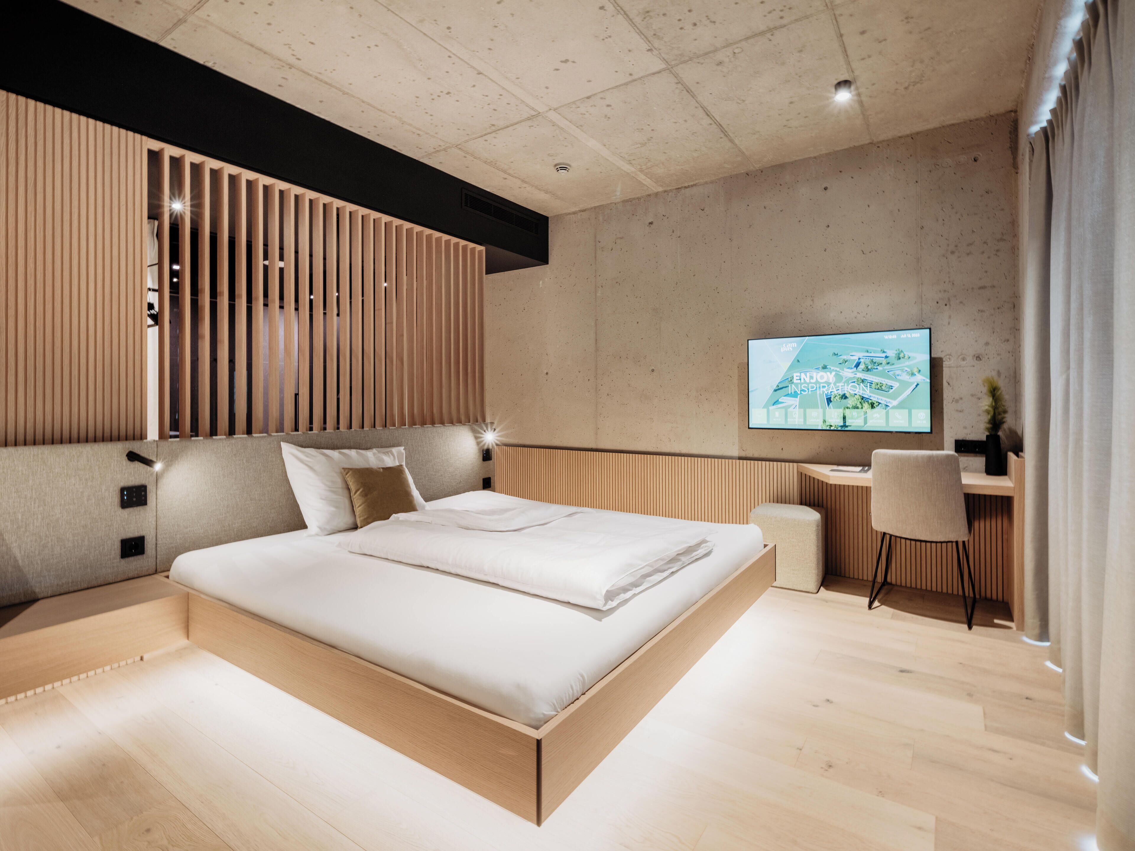 A modern bedroom with a wooden bed, a desk, and a TV on the wall.