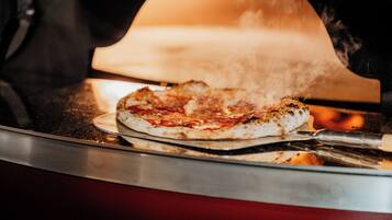 A pizza in a wood-fired oven with steam rising from it.