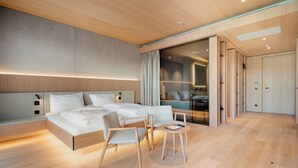Une chambre d’hôtel moderne dotée d’un grand lit, d’un coin salon avec une petite table et d’une salle de bain visible à travers une porte coulissante.