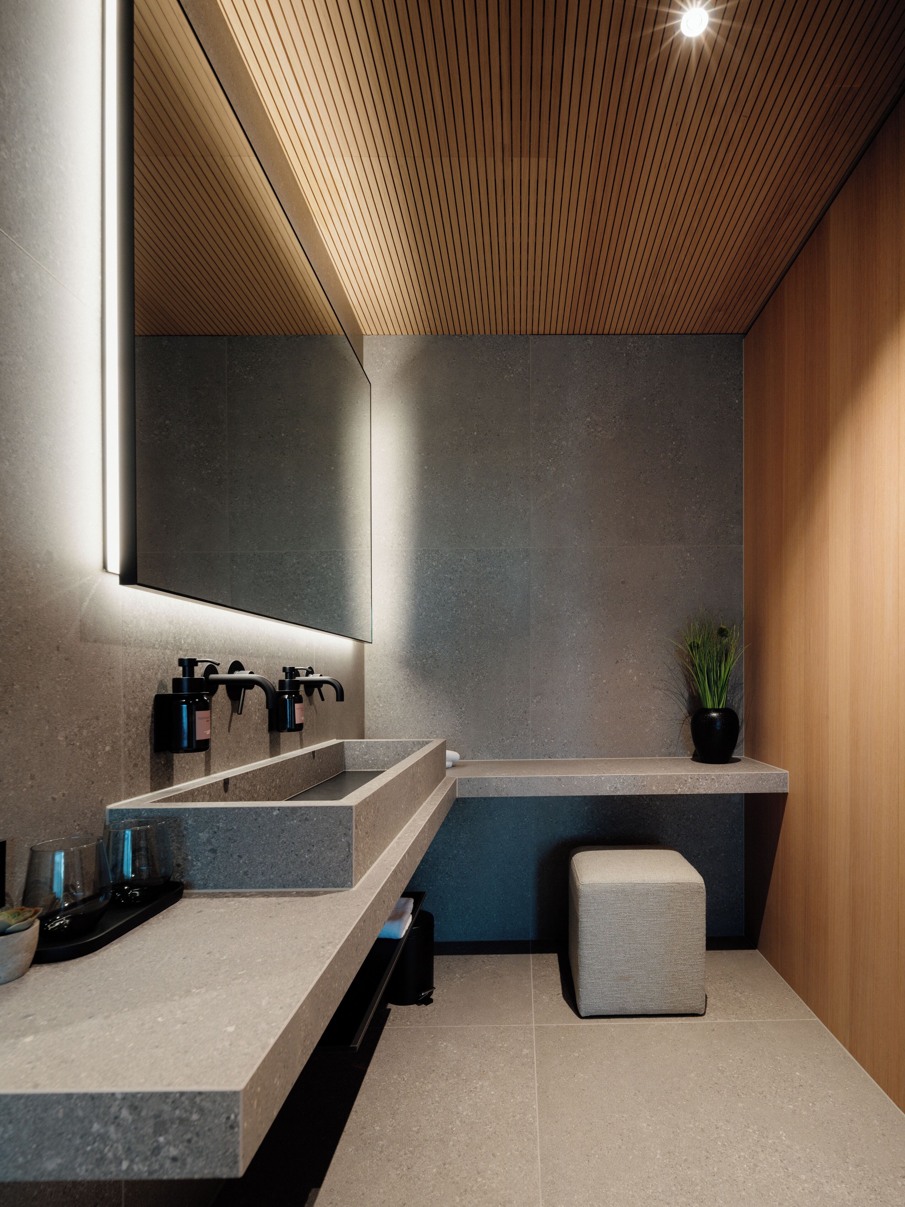 Een moderne badkamer met een houten plafond, een grote spiegel, een wastafelmeubel met dubbele wastafel, een klein bankje en een pot met plant.