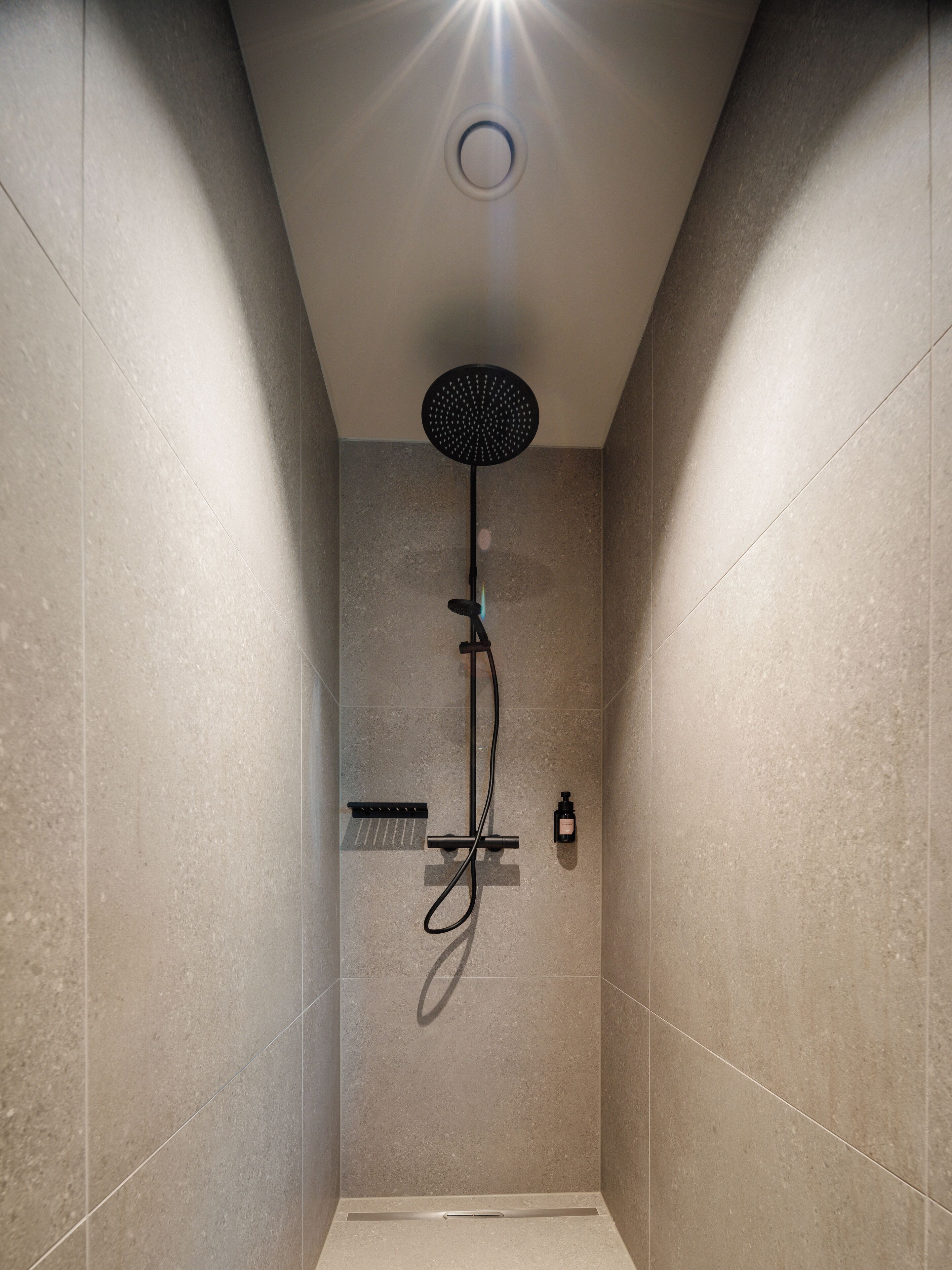Une douche moderne dotée d’un pommeau de douche rond, d’un pommeau de douche à main et d’un distributeur de savon à main.