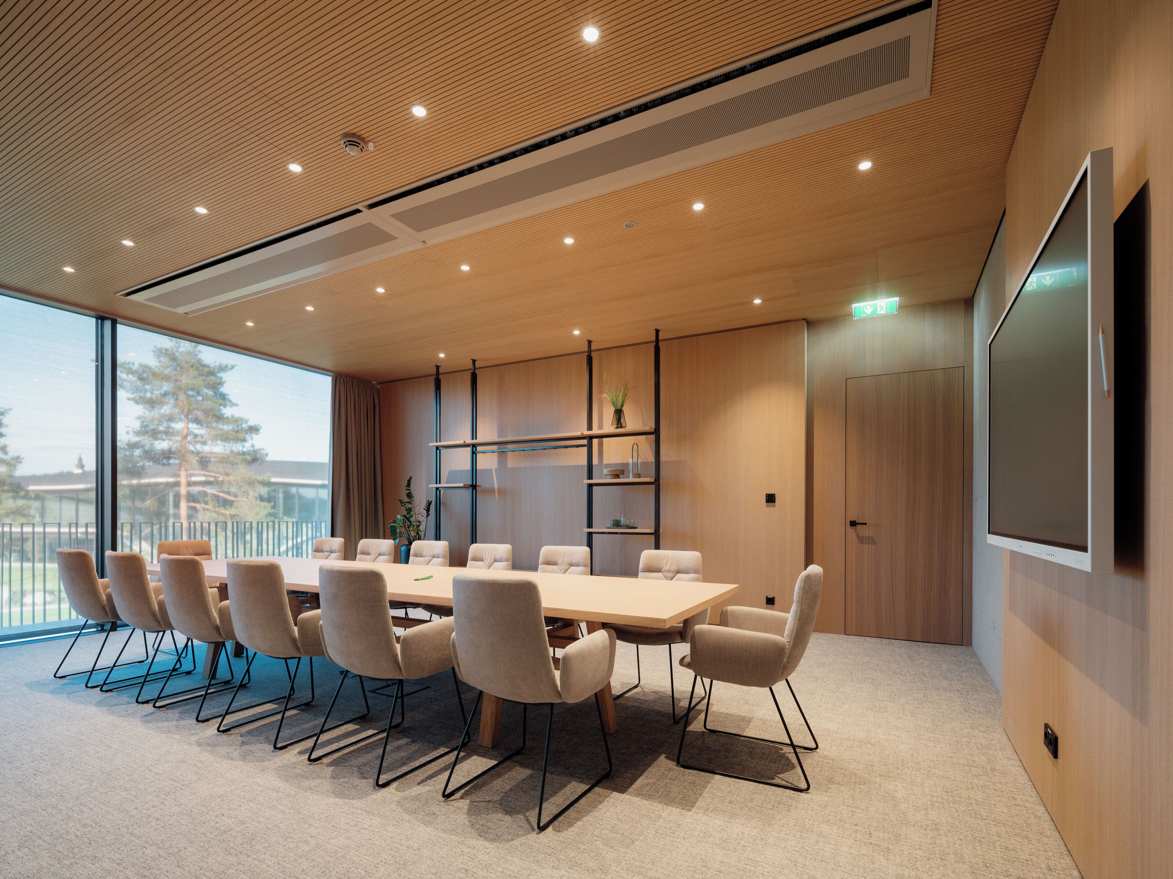 Un salón de conferencias con una gran mesa, sillas, una pantalla de proyector y vistas al exterior.