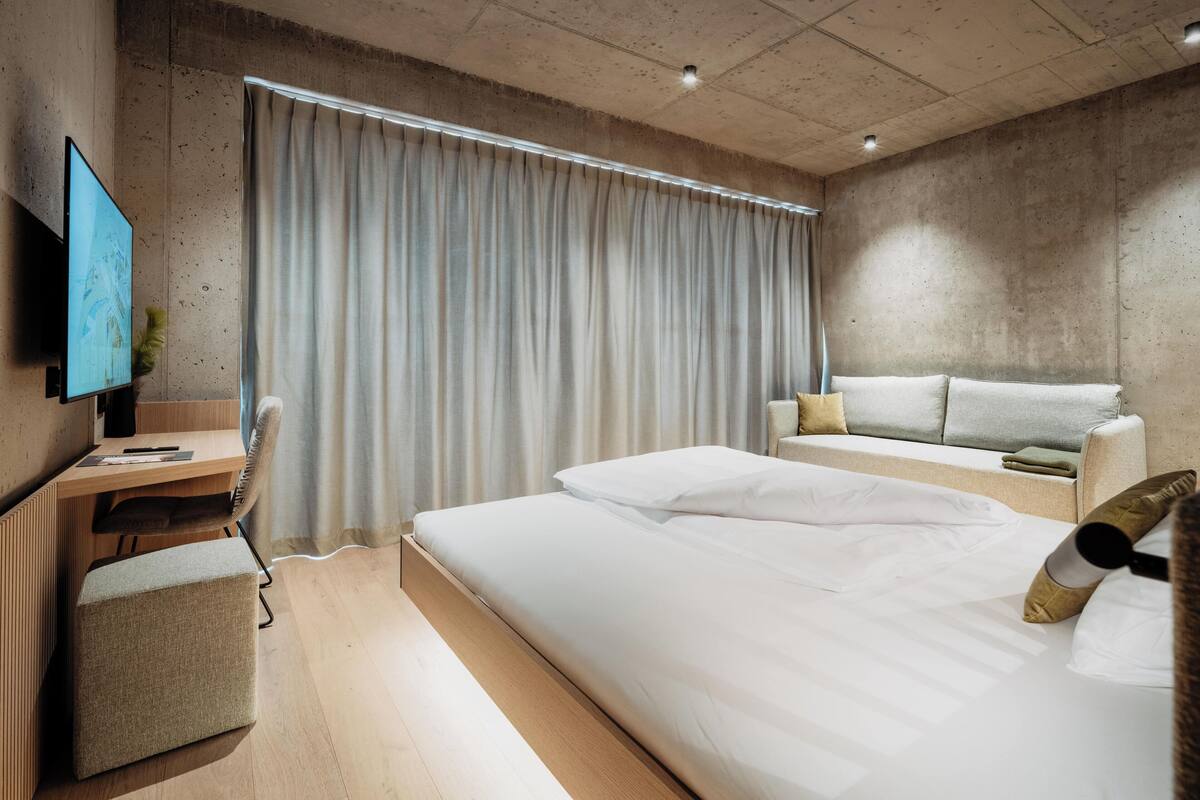 A modern hotel room with a large bed, a desk, a sofa, and a TV.