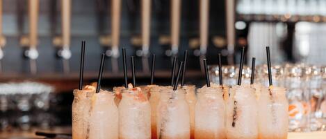 Un bar con varios vasos de bebidas heladas con pajitas, una barra de madera y un fondo borroso de estanterías.