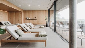 Un spa moderne avec des murs lambrissés, de nombreux transats avec des serviettes et une vue sur l’extérieur grâce à de grandes fenêtres.