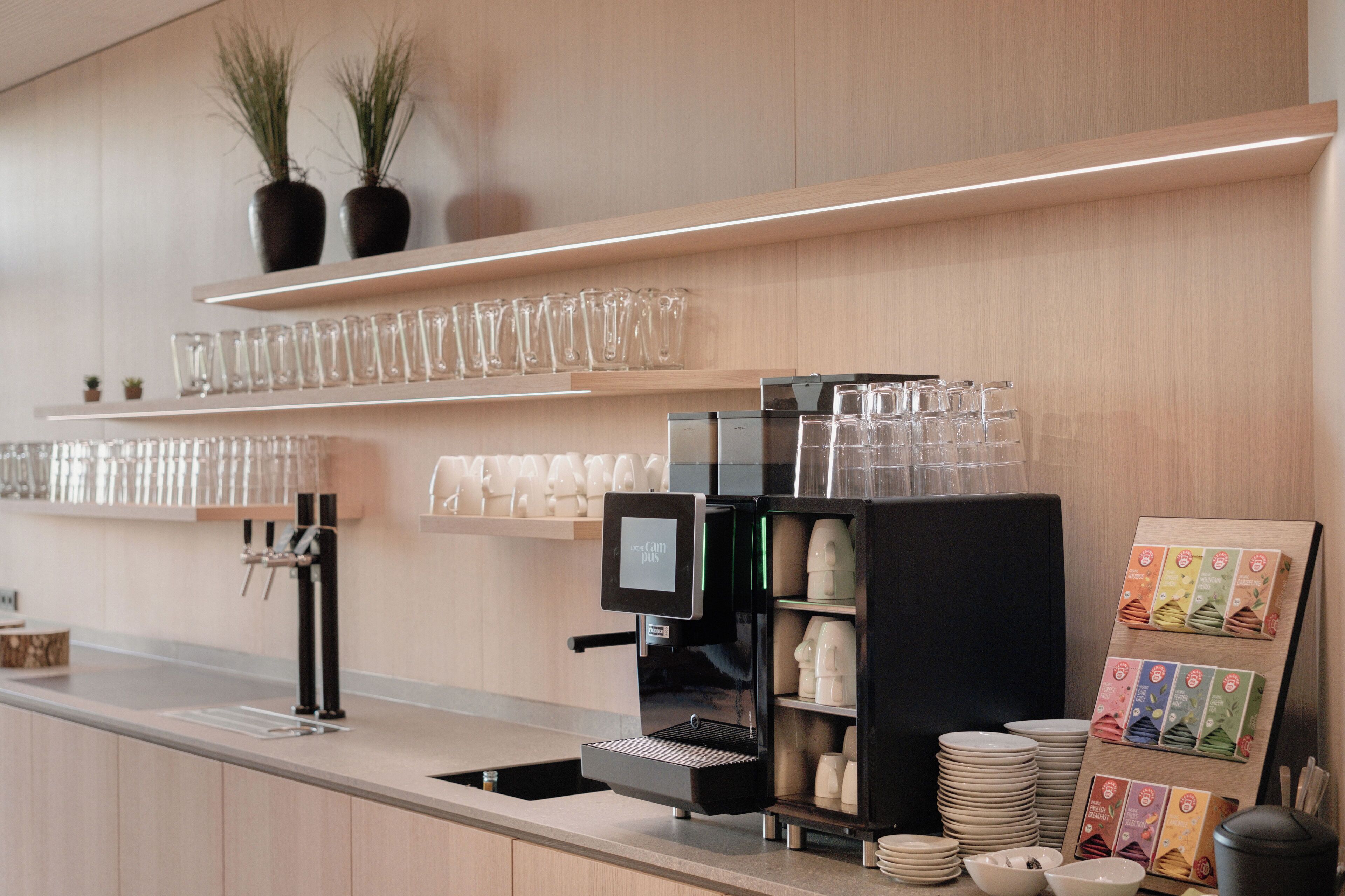 A modern coffee station with a coffee machine, glassware, and neatly arranged beverage dispensers.