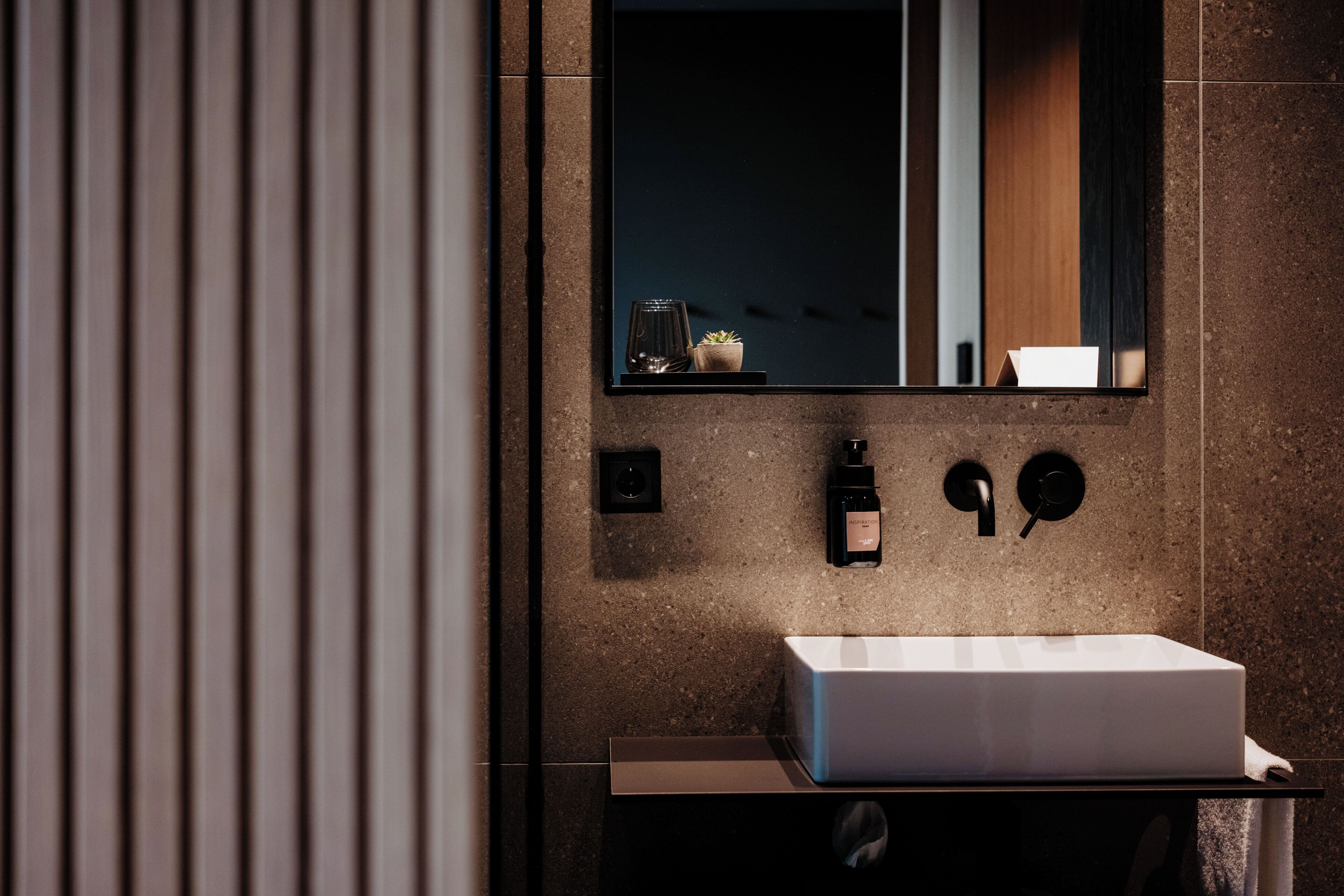 Un bany modern amb un lavabo rectangular, un mirall i una petita planta en test.