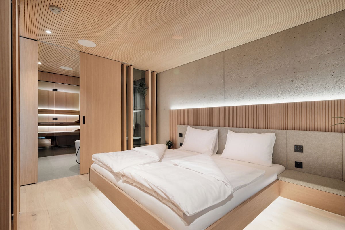 A modern bedroom with a large bed, wooden headboard, and built-in lighting.