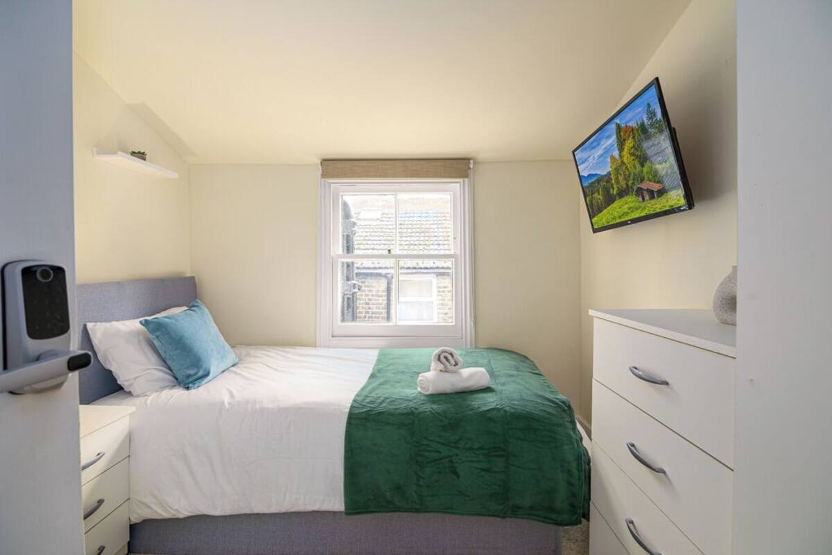 Une chambre à coucher avec un lit, une fenêtre, une commode et un téléviseur fixé au mur.
