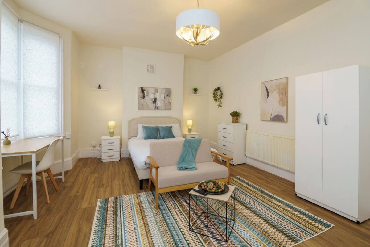 Une chambre bien éclairée, avec un lit, des tables de chevet, un bureau, une armoire et un tapis à motifs.