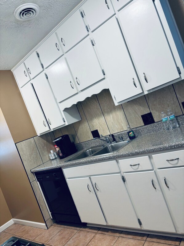 A kitchen with white cabinets, a granite countertop, and a dishwasher. - Convenient, and Clean Home 1BR (Springdale)