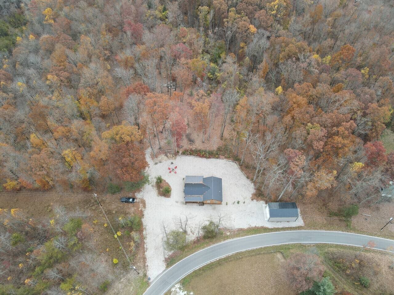 An aerial view of a property with a house surrounded by autumn-colored trees, a driveway, and a road curving around the property.