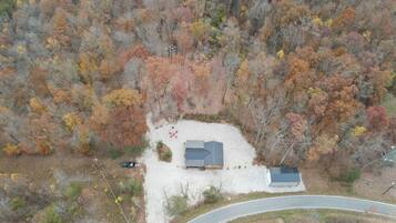 An aerial view of a property with a house surrounded by autumn-colored trees, a driveway, and a road curving around the property.