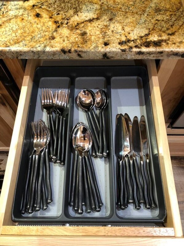 A drawer containing a set of black cutlery including forks, spoons, and knives.