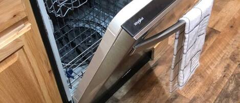 An open dishwasher in a kitchen with wooden cabinets and a patterned rug on the floor.