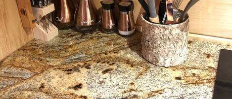 Una encimera de granito, una cafetera, un bloque de cuchillos y una espejeria.