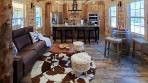 A log cabin interior with a central island dining area, a sofa, and a round rug with a cowhide pattern.