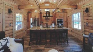 A log cabin interior with a central island kitchen, wooden walls, and large windows.