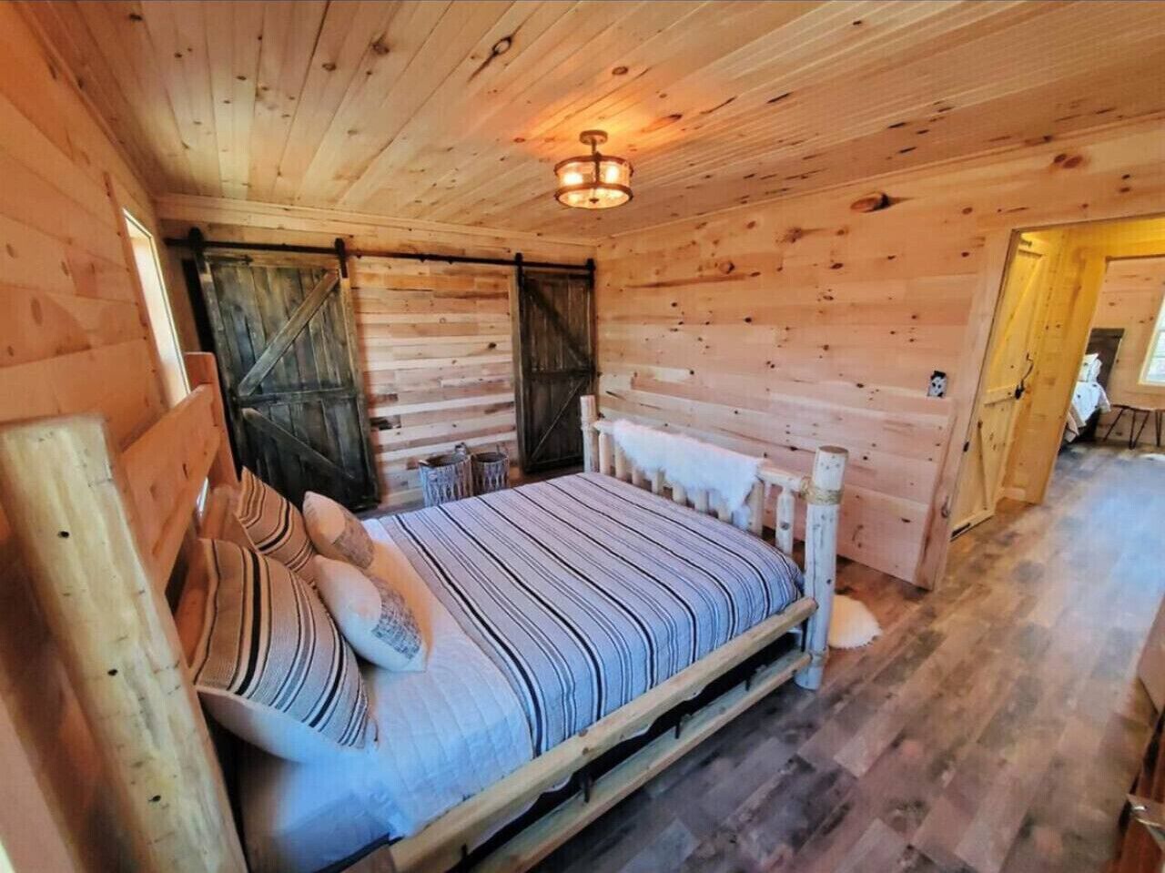 Camera da letto in una baita di legno, con un letto, cuscini e una lampada a sospensione.