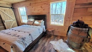 A wooden cabin bedroom with a bed, windows, and a rustic barrel.