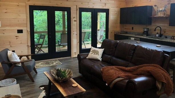 A cozy cabin interior with a leather sofa, a dining table, and a kitchen area.