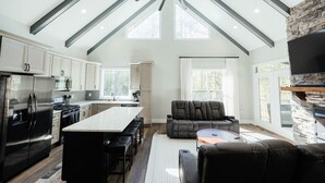 A modern kitchen with a central island, a dining area with a black leather couch, and a stone fireplace. - Cedar Ridge Red River Gorge HotTub WiFi (Campton)