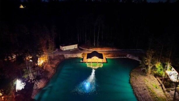 A nighttime view of a swimming pool with a small building in the center, surrounded by trees. - Cedar Ridge Red River Gorge HotTub WiFi (Campton)