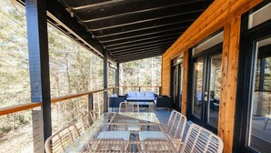 Een overdekt terras met een tafel en stoelen, met uitzicht op een bebost gebied.