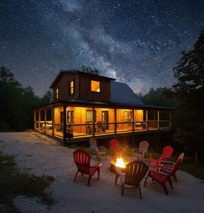 A wooden cabin with a deck, outdoor seating, and a fire pit under a starry night sky.