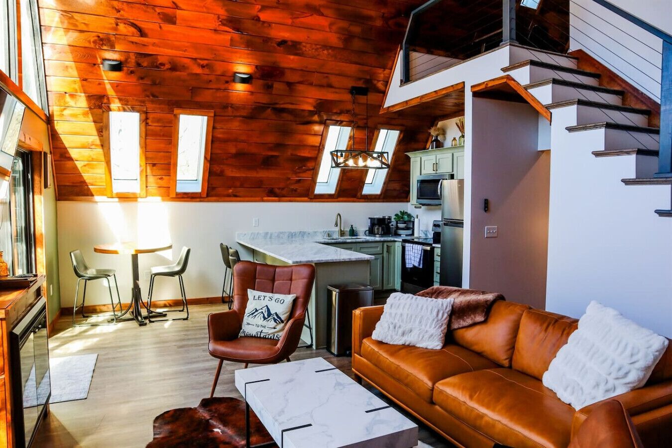 A cozy interior with a wooden ceiling, a dining area, a sofa, and a kitchen.