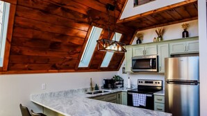Una cocina con encimera de mármol, techo de madera y electrodomésticos modernos.