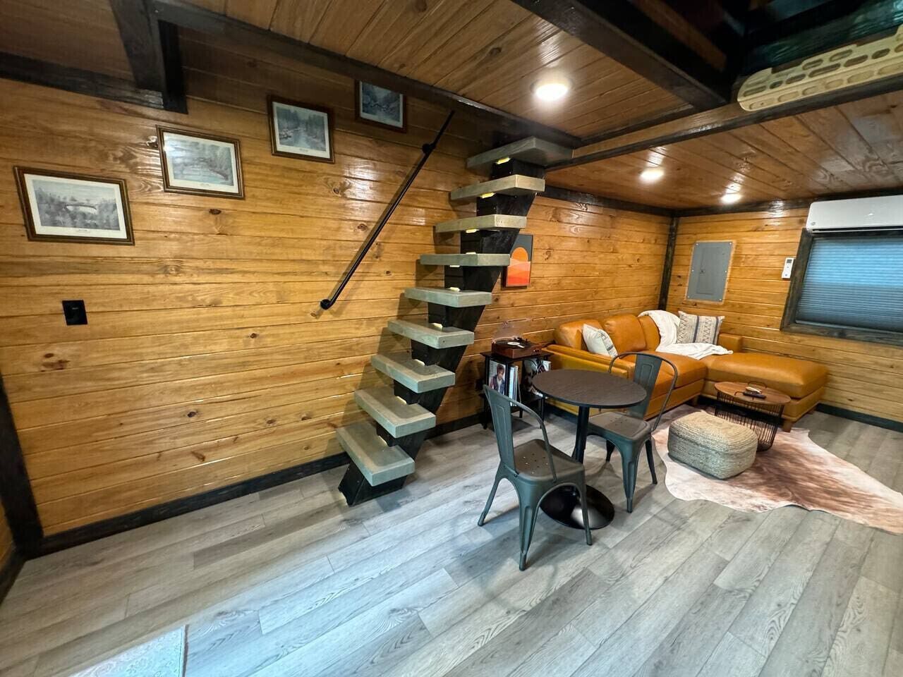 Un intérieur en bois avec un escalier, un canapé, une table et un tapis.