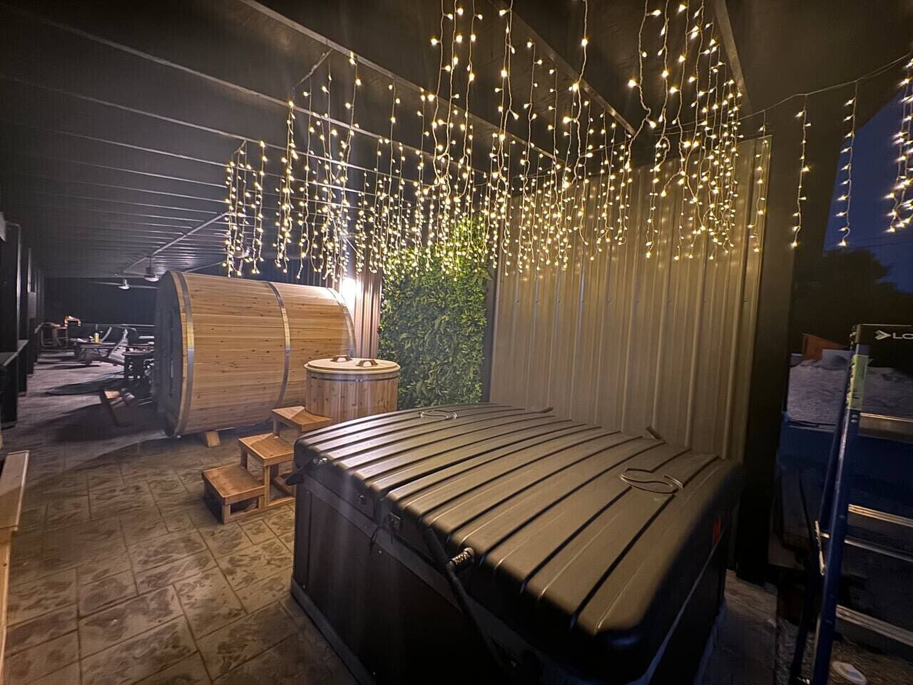Una sauna con una grande botte di legno, un lettino da massaggio e luci decorative appese.