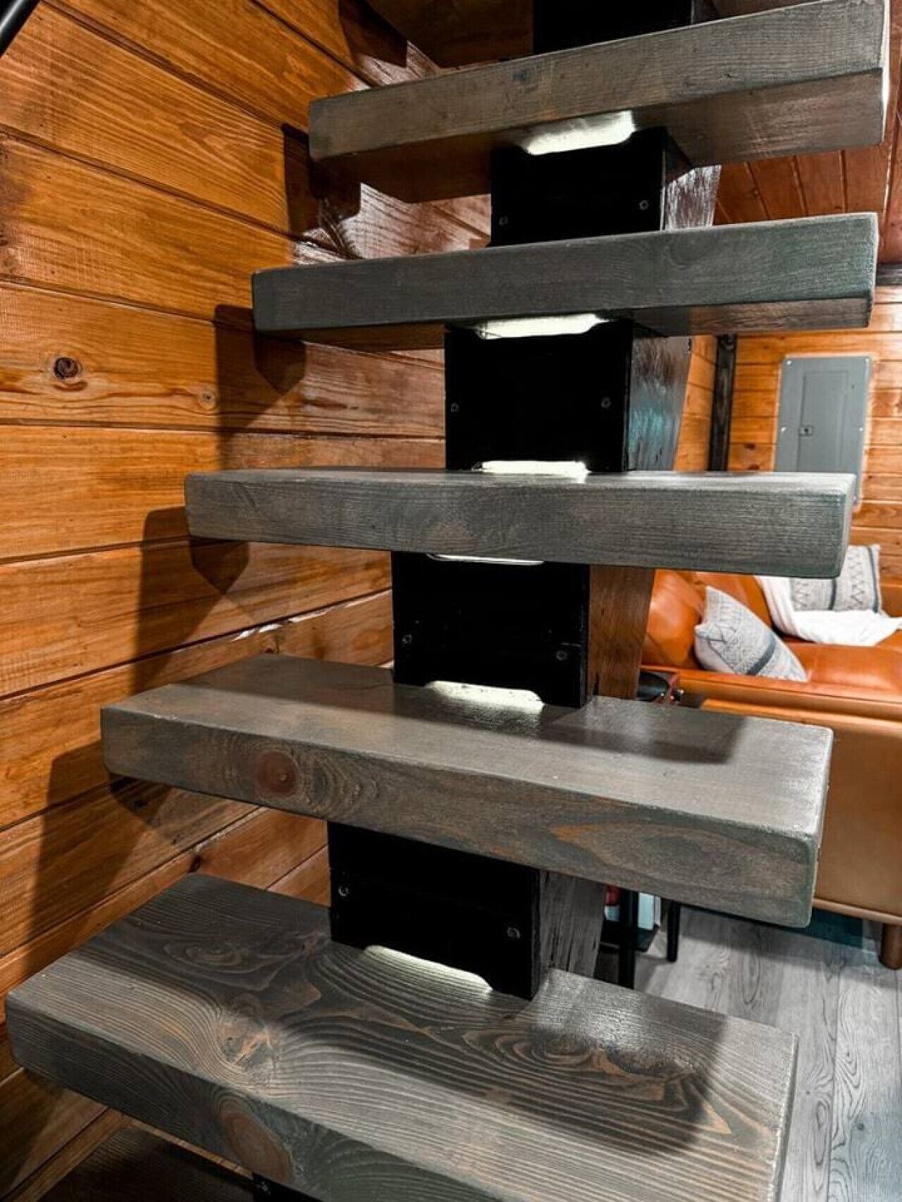 A staircase with wooden steps and metal supports, leading to a room with a leather sofa and a wooden floor.