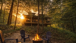 A cabin with a fire pit and Adirondack chairs in a forest setting.