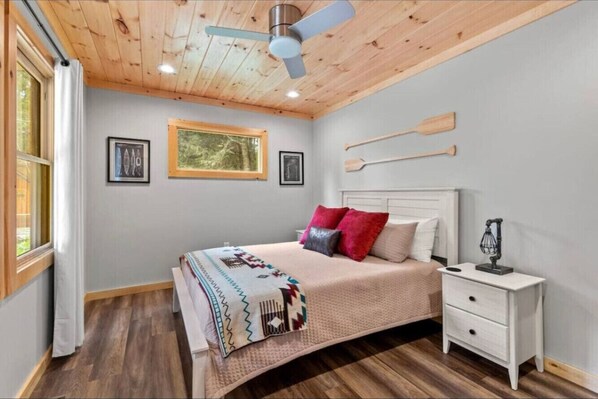 Ein Schlafzimmer mit Holzbalkendecke, einem Bett mit gemustertem Überwurf, einem Nachttisch und zwei gerahmten Bildern an der Wand.