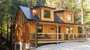 Eine Holzhütte mit Veranda und Steinfundament, umgeben von Bäumen.