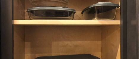 A cabinet with three glass baking dishes on shelves.